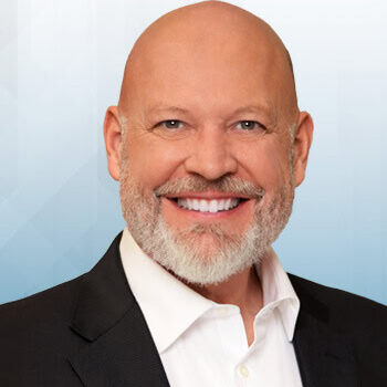 A headshot-style photo of a man smiling towards you